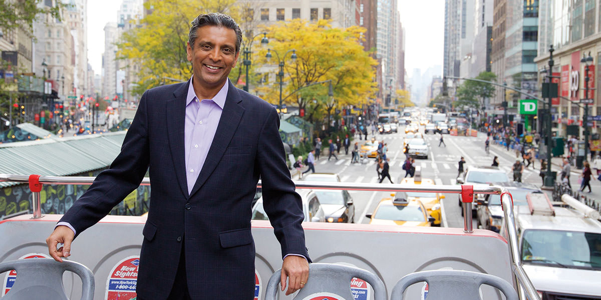 Raj Subramaniam standing on an open-top sightseeing bus with a busy city street behind him