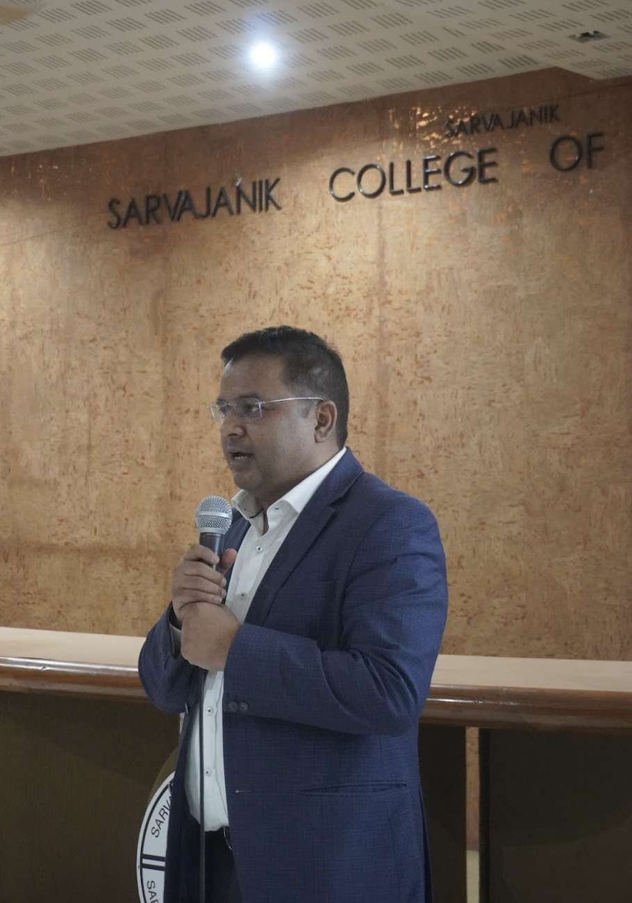 Ramendra Shukla holding a microphone while speaking at SCET in Surat