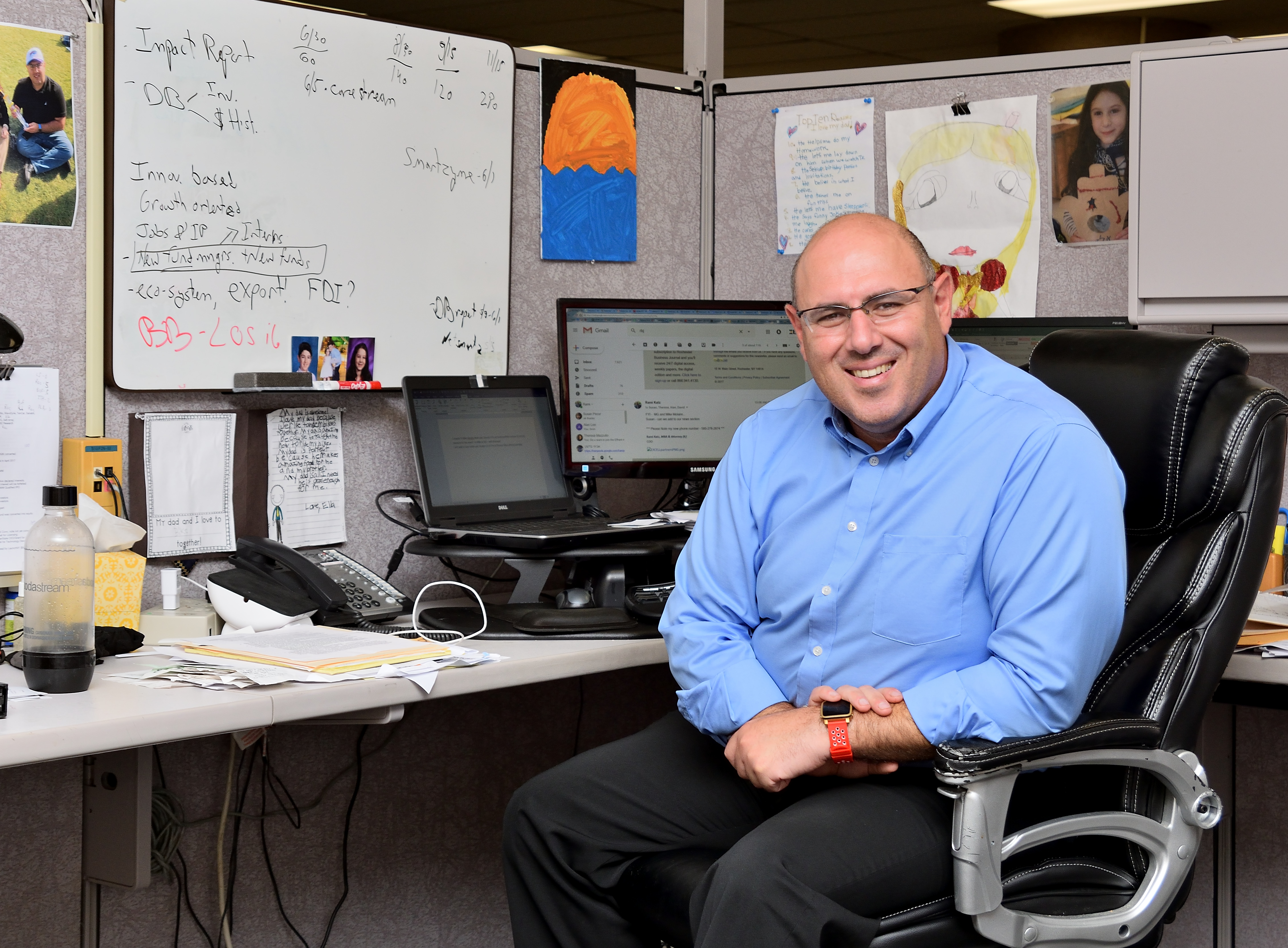 Rami Katz seated at his desk in Excell's Kodak Tower office, with a whiteboard and drawings behind him