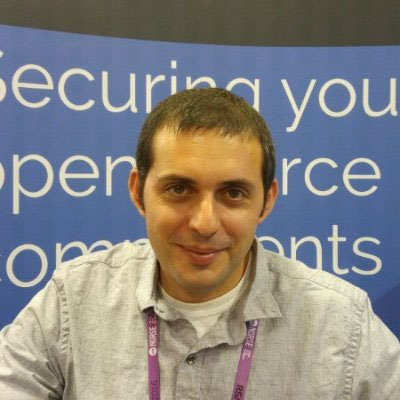 Rami Sass wearing a conference lanyard in front of a WhiteSource open source security display