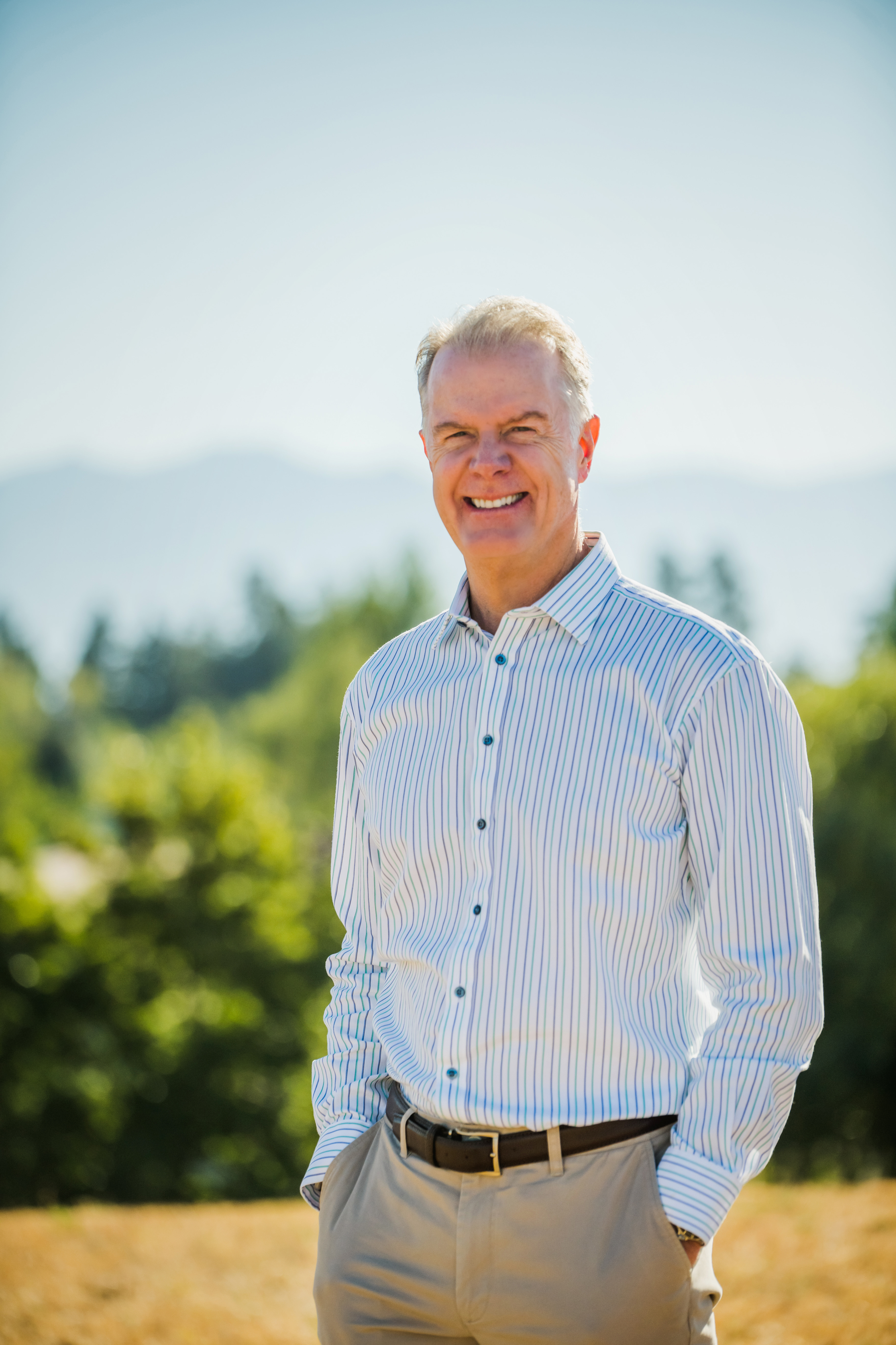 Randy Chesler outdoors in a striped shirt, with trees and mountains behind him