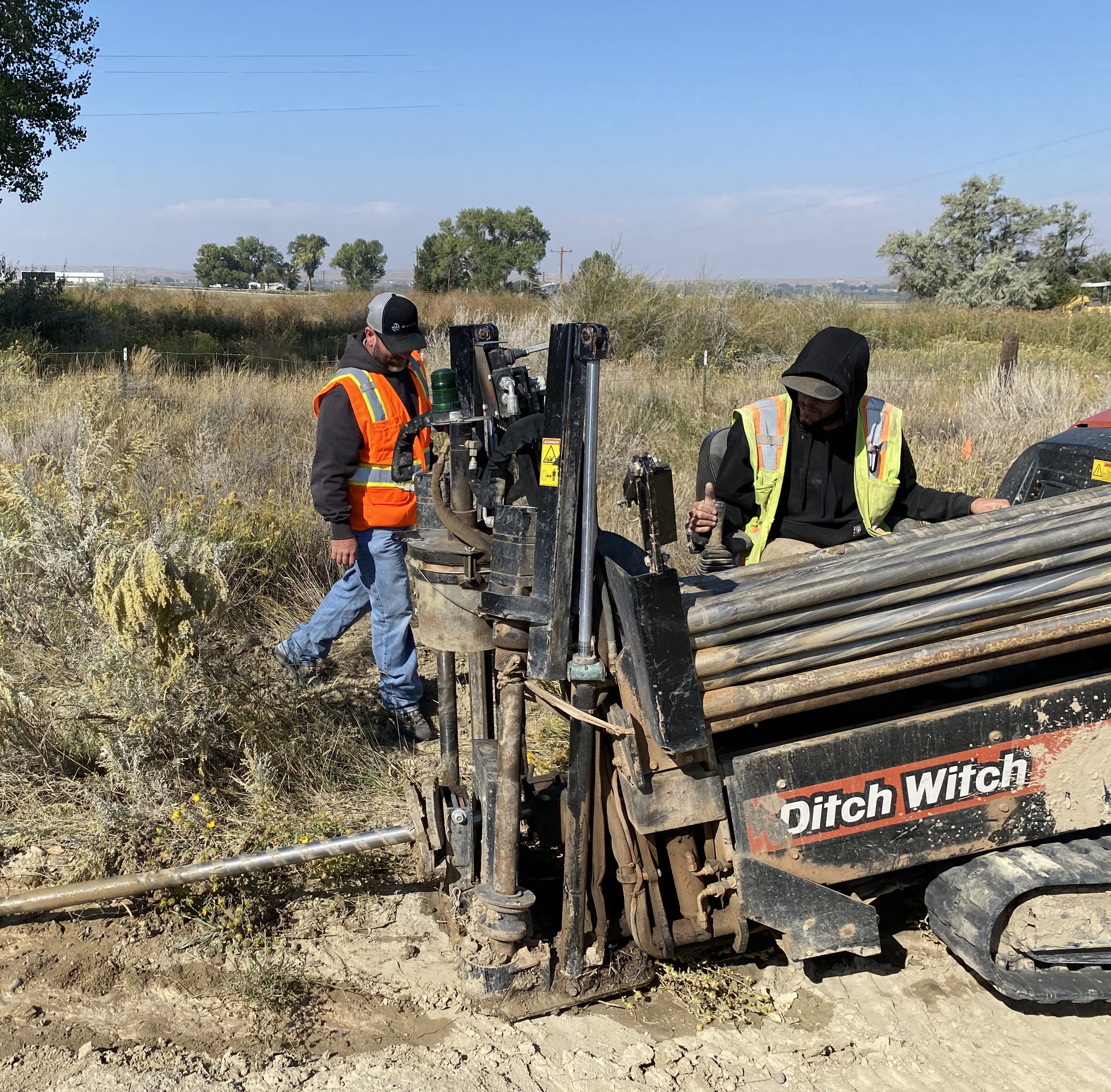 Two construction workers operating a directional drilling machine beside an open field
