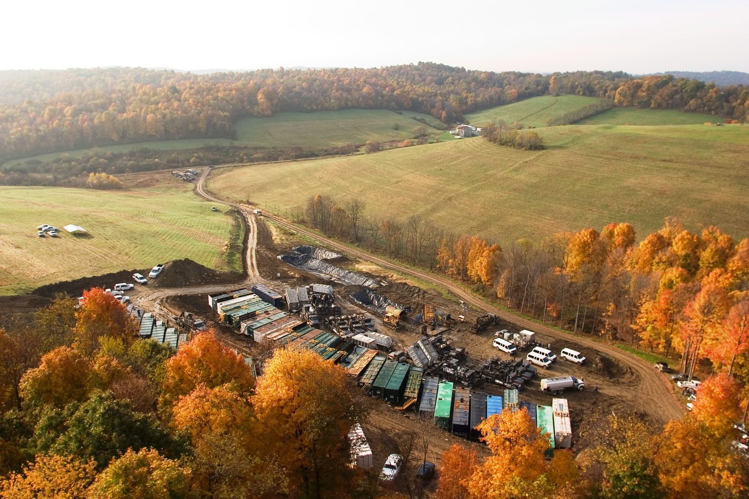 Archival aerial photograph of well-site equipment surrounded by autumn fields and trees
