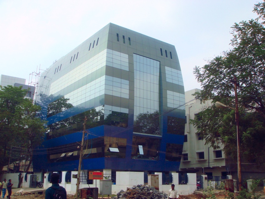 Glass-fronted Qatalys offshore development centre building in Chennai, with trees and street activity in front