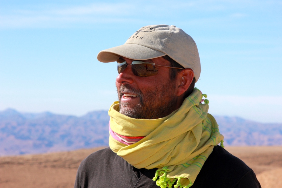 Raoul Pal wearing sunglasses and a cap in a desert landscape