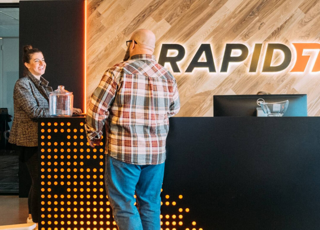 Two people talking at the reception desk inside a Rapid7 office