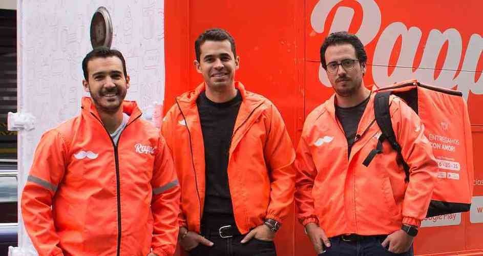 Rappi’s three founders wearing orange jackets beside a branded delivery vehicle