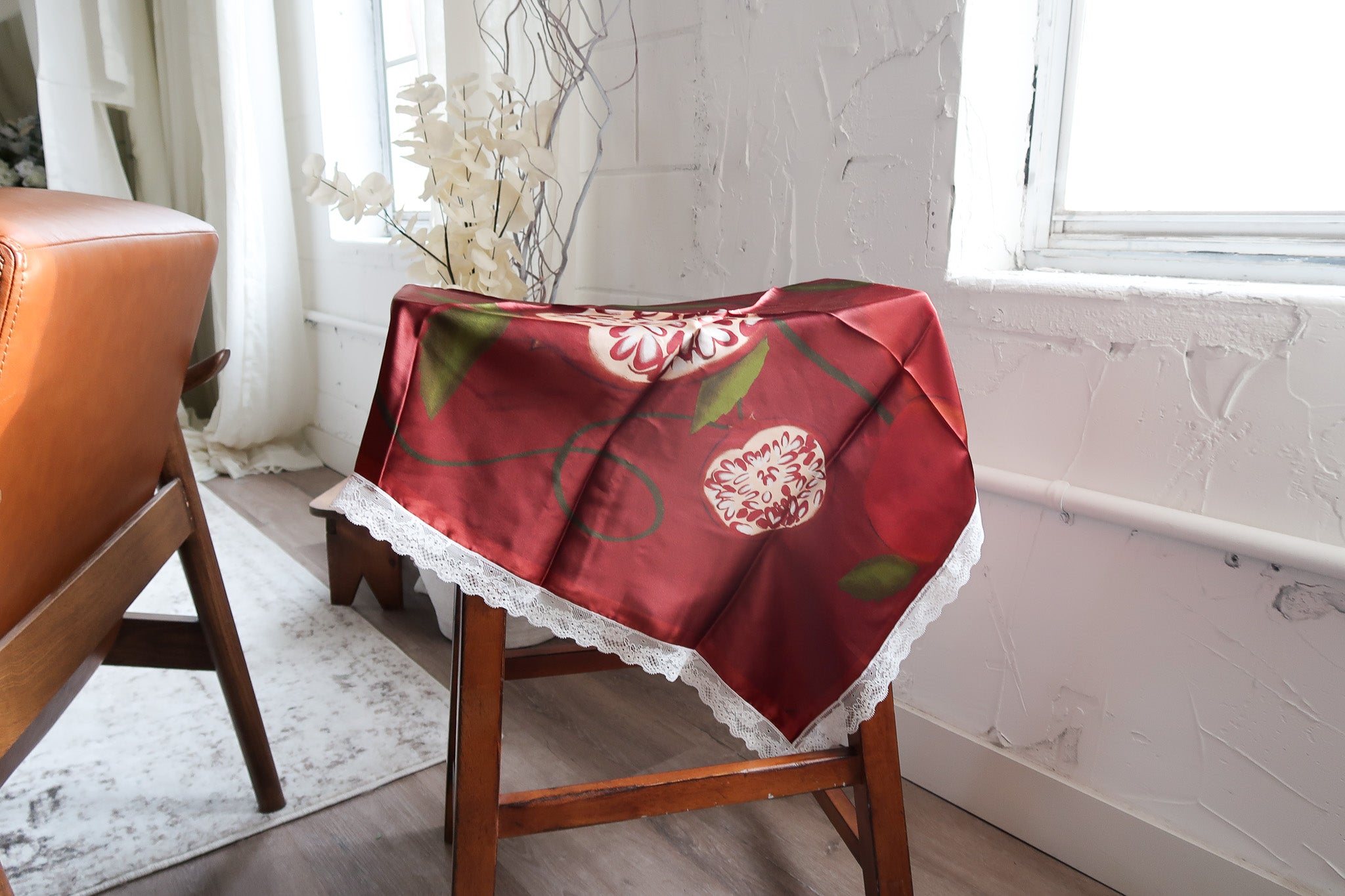 A burgundy illustrated silk scarf draped over a wooden chair in a bright studio