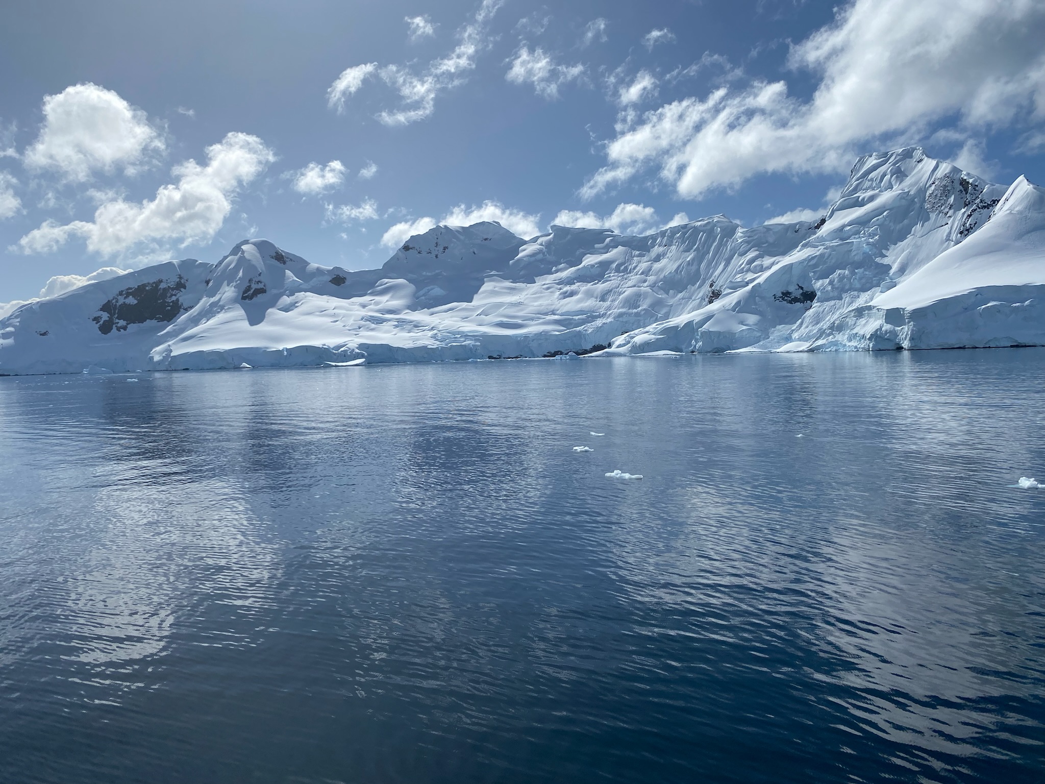 A bright Antarctic ice shelf reflected in calm blue water beneath scattered clouds