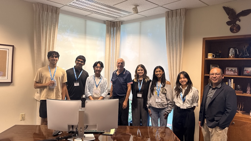 Ray Melissa standing with student visitors and a colleague behind his office desk