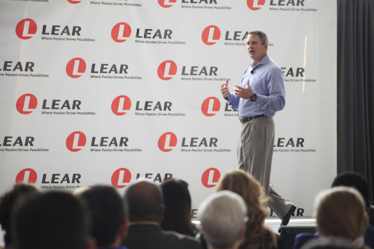 Ray Scott speaking on a stage at Lear’s Flint facility, with an audience in the foreground