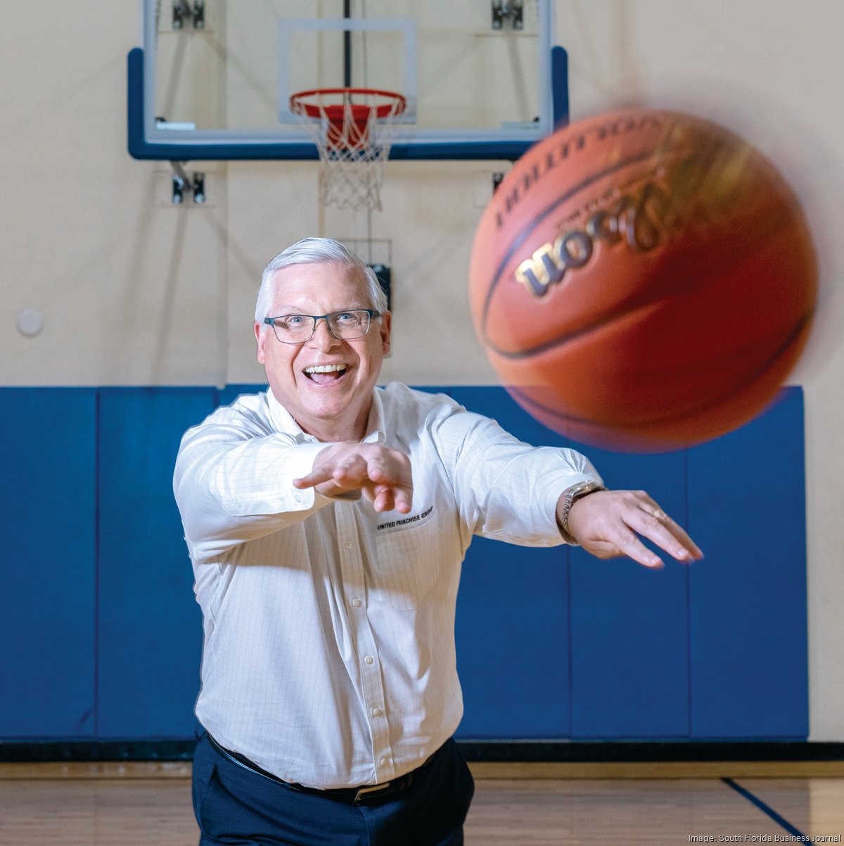 Ray Titus smiling as he tosses a basketball towards the camera on an indoor court