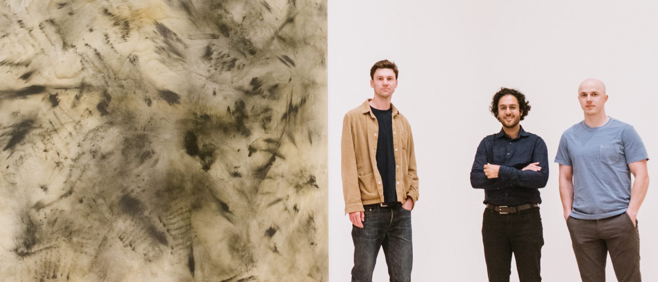 Humanloop's three co-founders standing beside a large abstract artwork, with Raza Habib in the centre