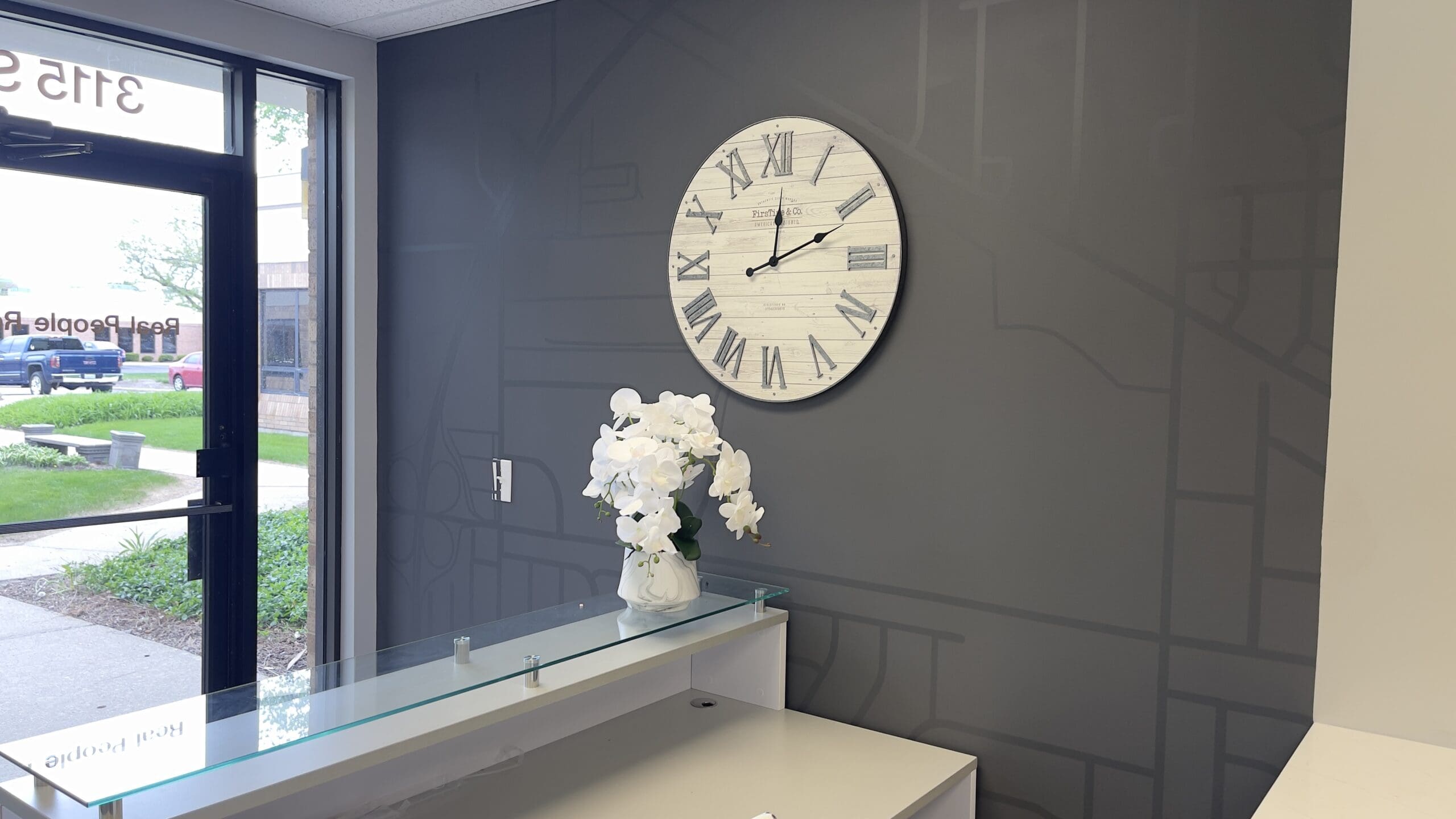 Reception area at Real People Realty’s Arlington Heights office, with a large wall clock and glass reception desk