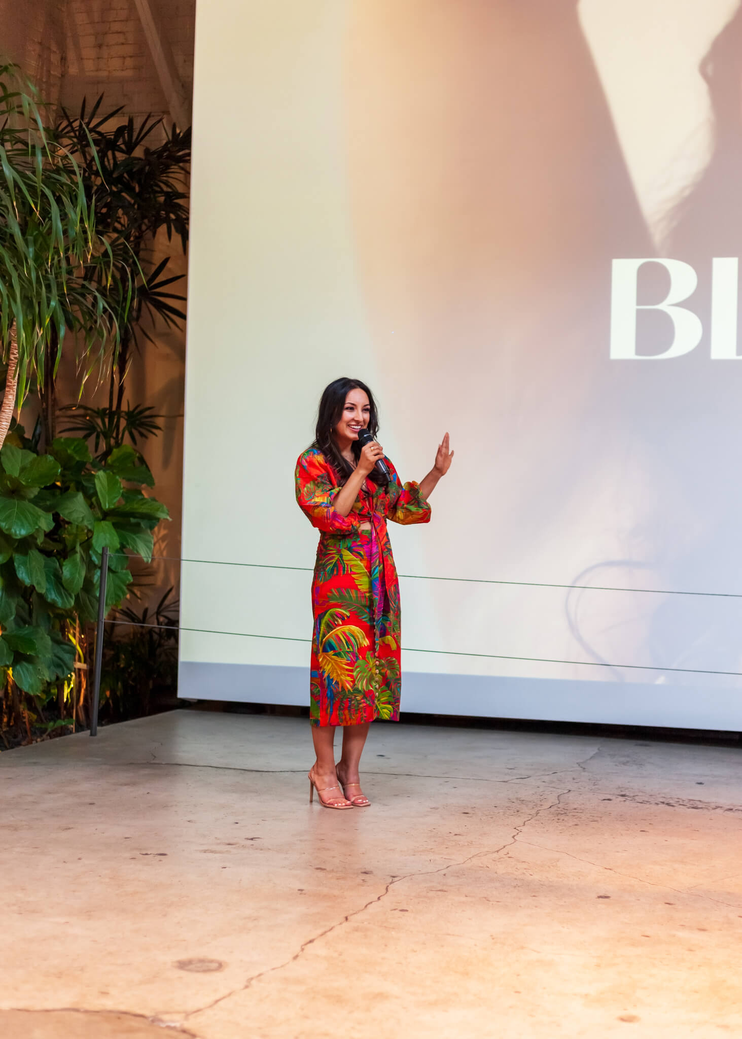Rebecca Alvarez Story speaking into a microphone in front of a Bloomi presentation