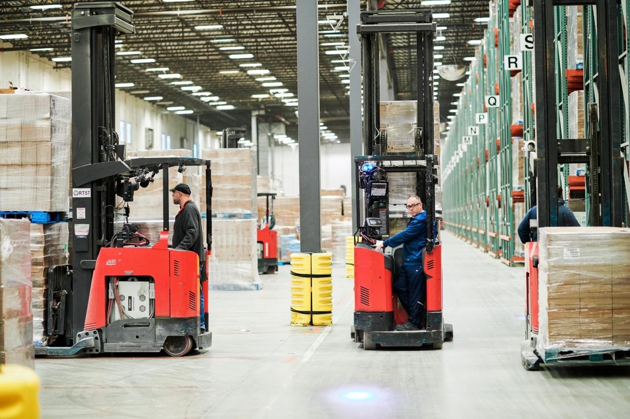 Forklift operators working between tall racks and stacked pallets in a warehouse