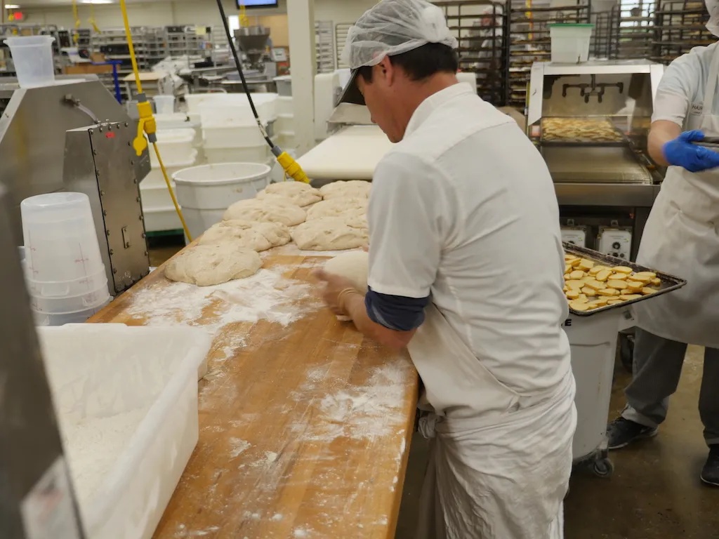 A baker shapes dough at a flour-covered table at Companion Baking