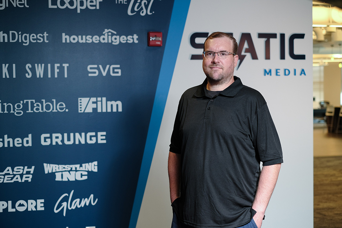 Reggie Renner standing in the Static Media office beside a wall of publication logos