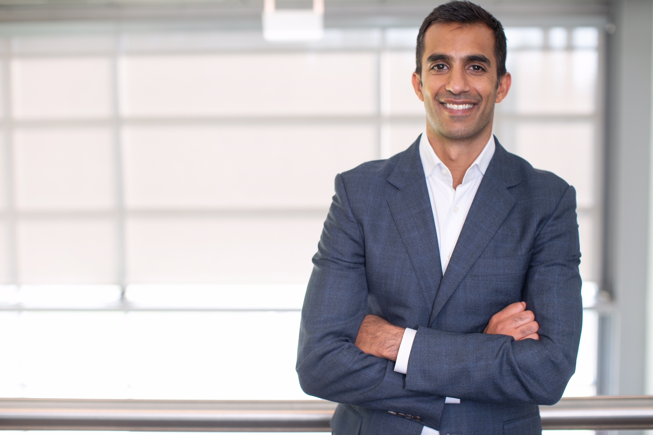 Rehan Verjee smiling with folded arms in an office, in the press photograph accompanying his 2018 appointment