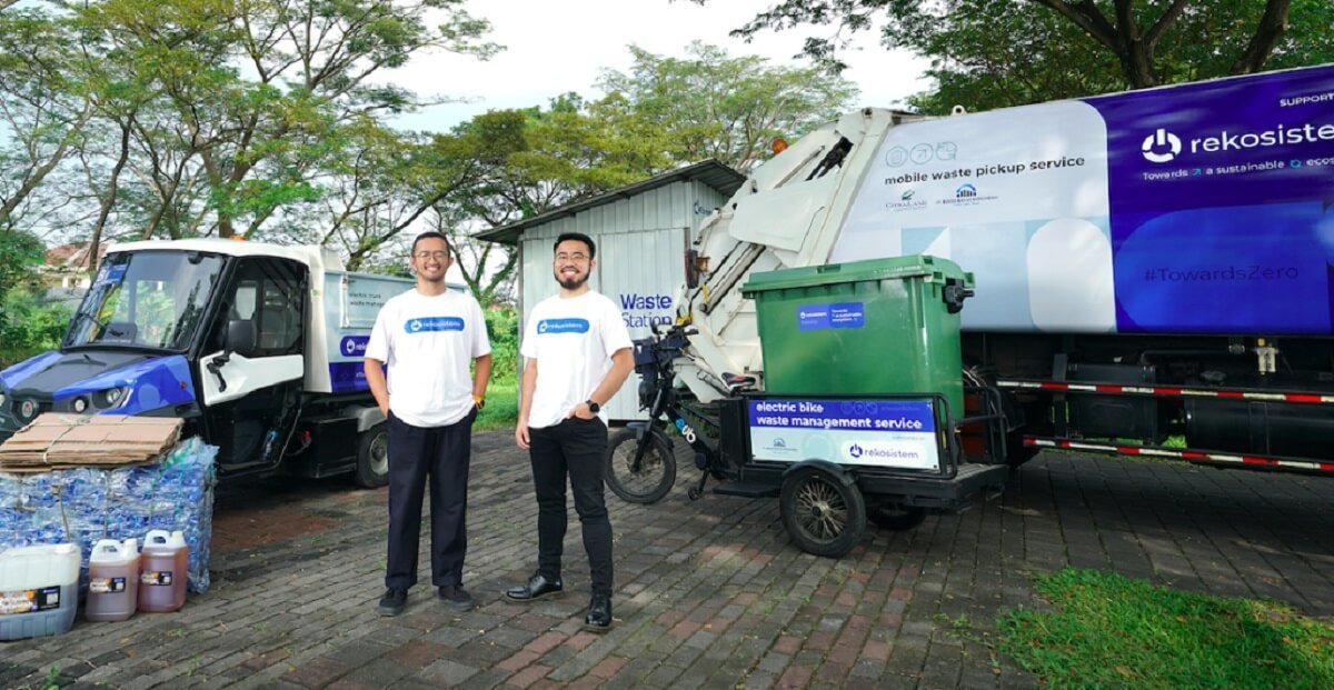 Rekosistem co-founders Ernest Layman and Joshua Valentino standing before the company's electric waste-collection fleet and a branded Waste Station truck