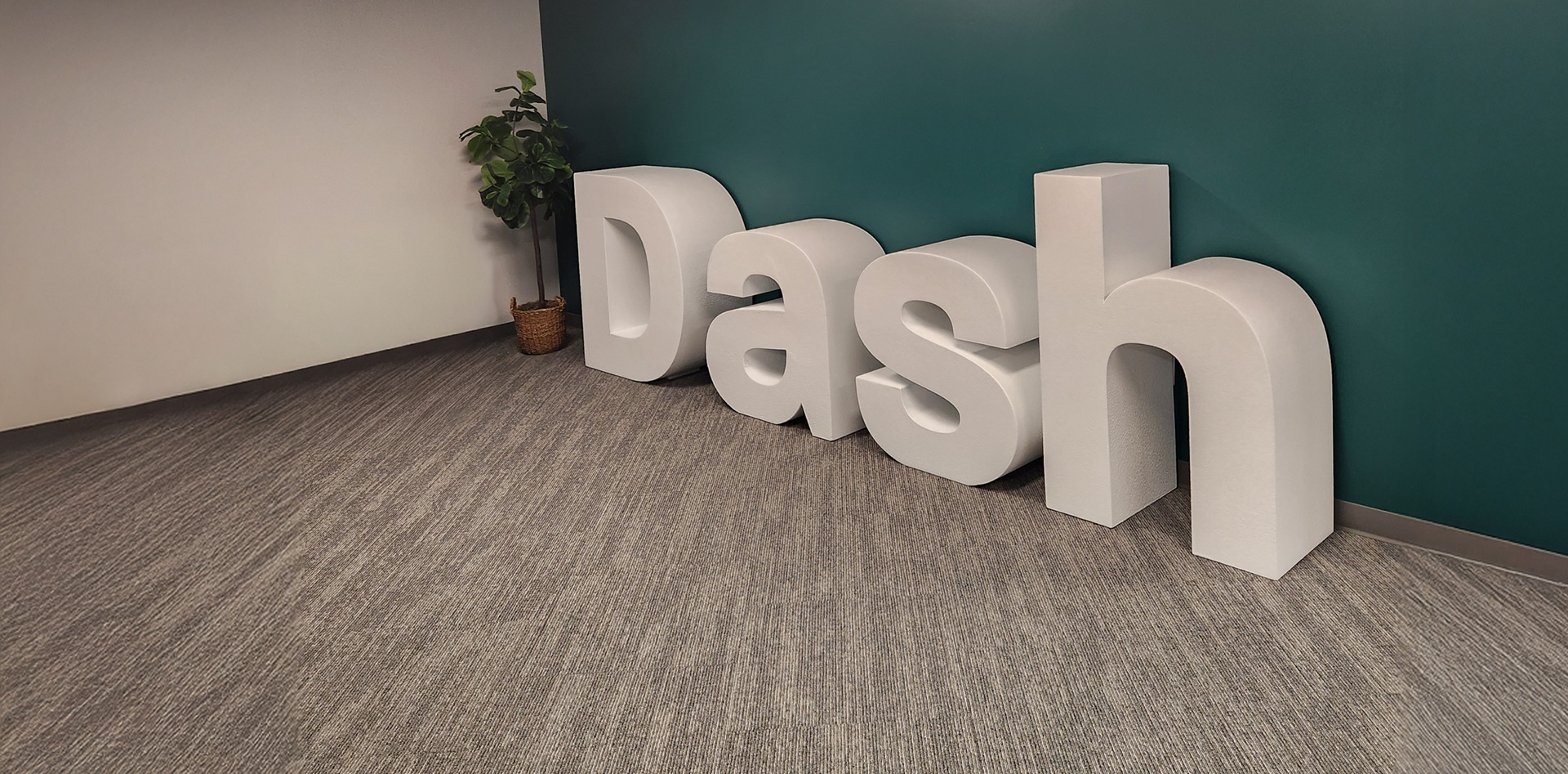 Oversized white Dash letters beside a plant against a green wall at Relatient’s Atlanta headquarters