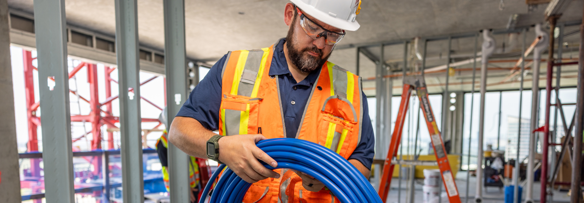 Installer carrying a coil of blue PEX pipe through a building under construction