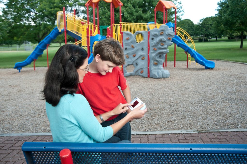 An adult helps a child use a handheld Spiro PD device outdoors
