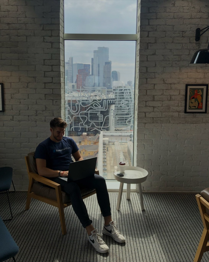 A RemoteMore team member working on a laptop beside a city window