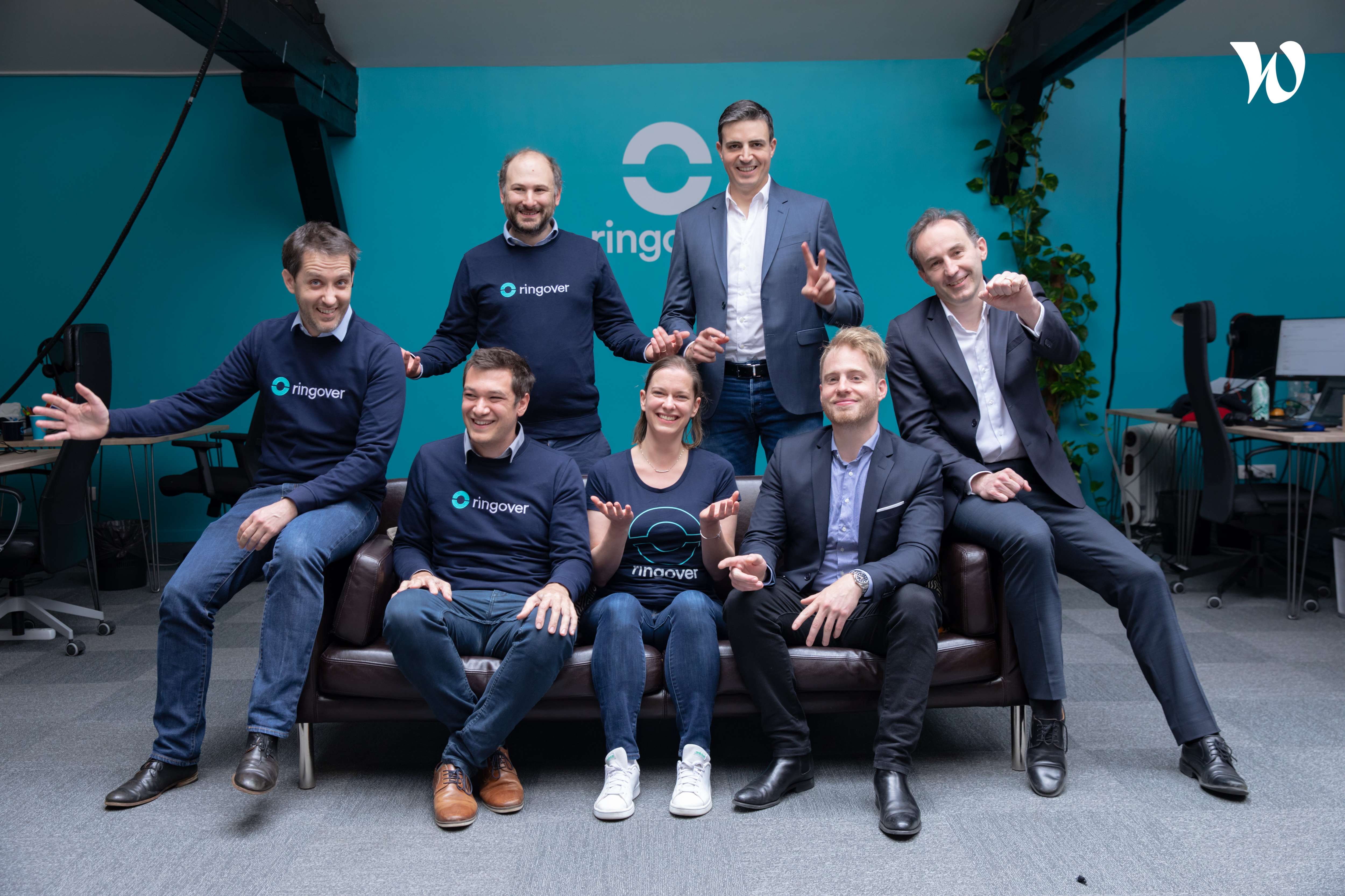 Members of the Ringover team pose together in an office in front of a Ringover sign