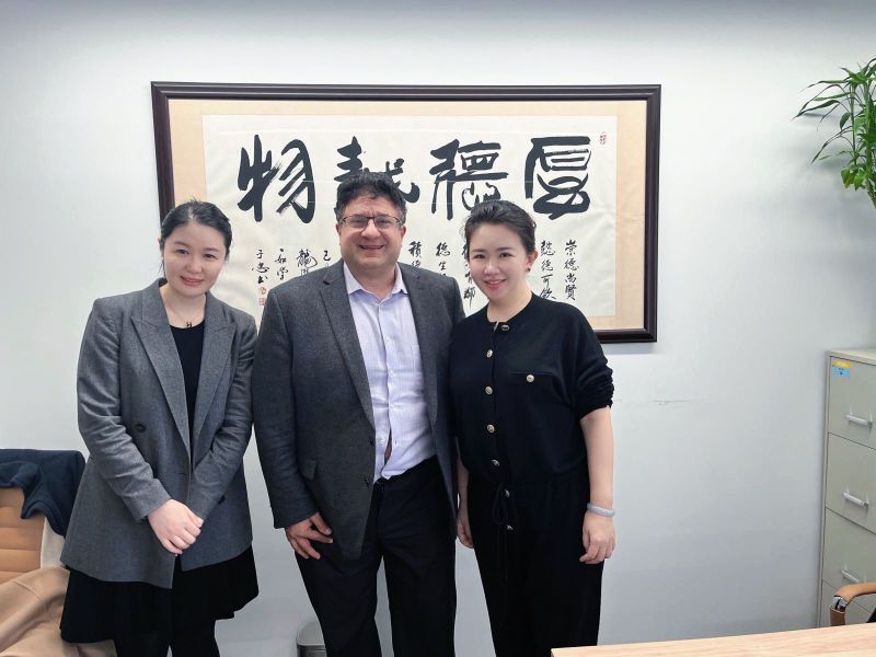 Three people, including Renee Li, standing in Alpha Square Group’s office beneath framed Chinese calligraphy