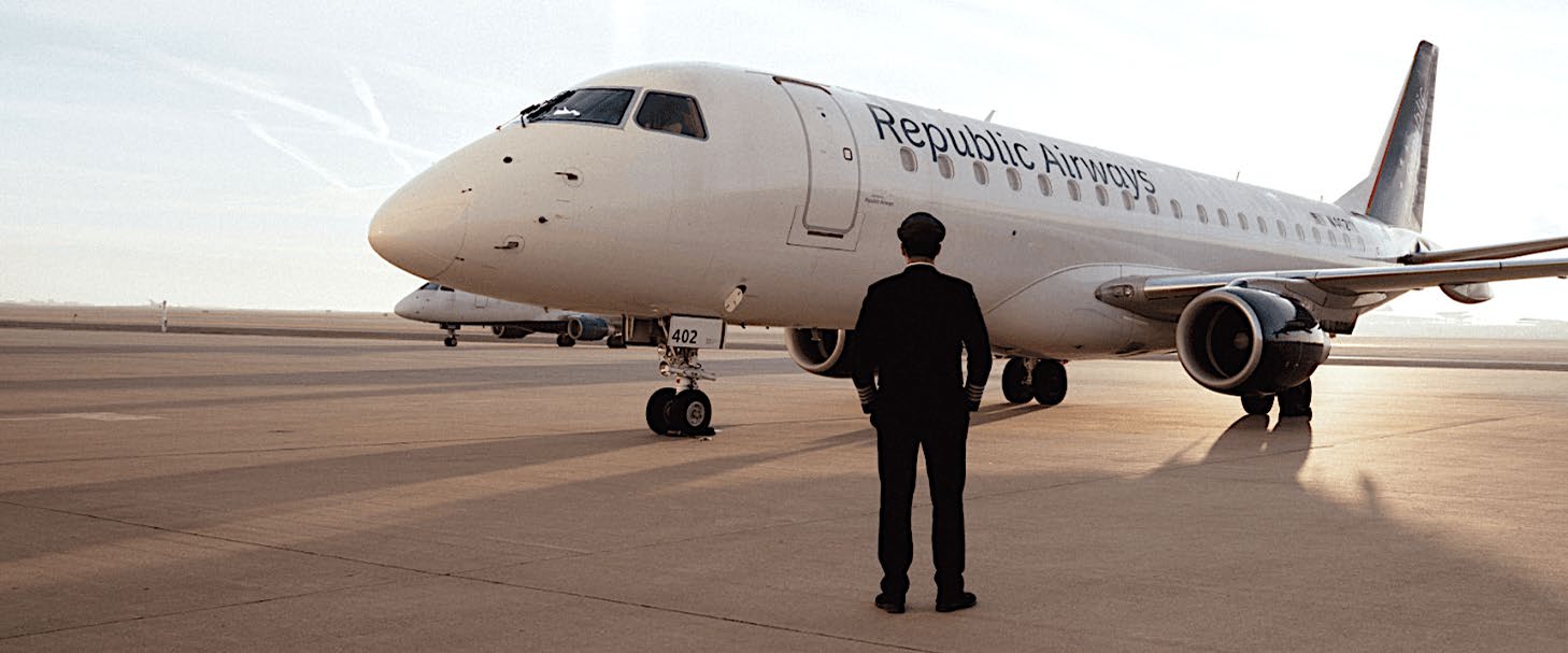 A uniformed pilot standing in front of a Republic Airways Embraer jet on an airport apron