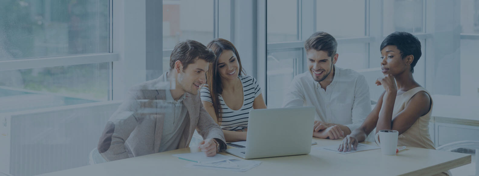 Four colleagues gathered around a laptop in a bright meeting room