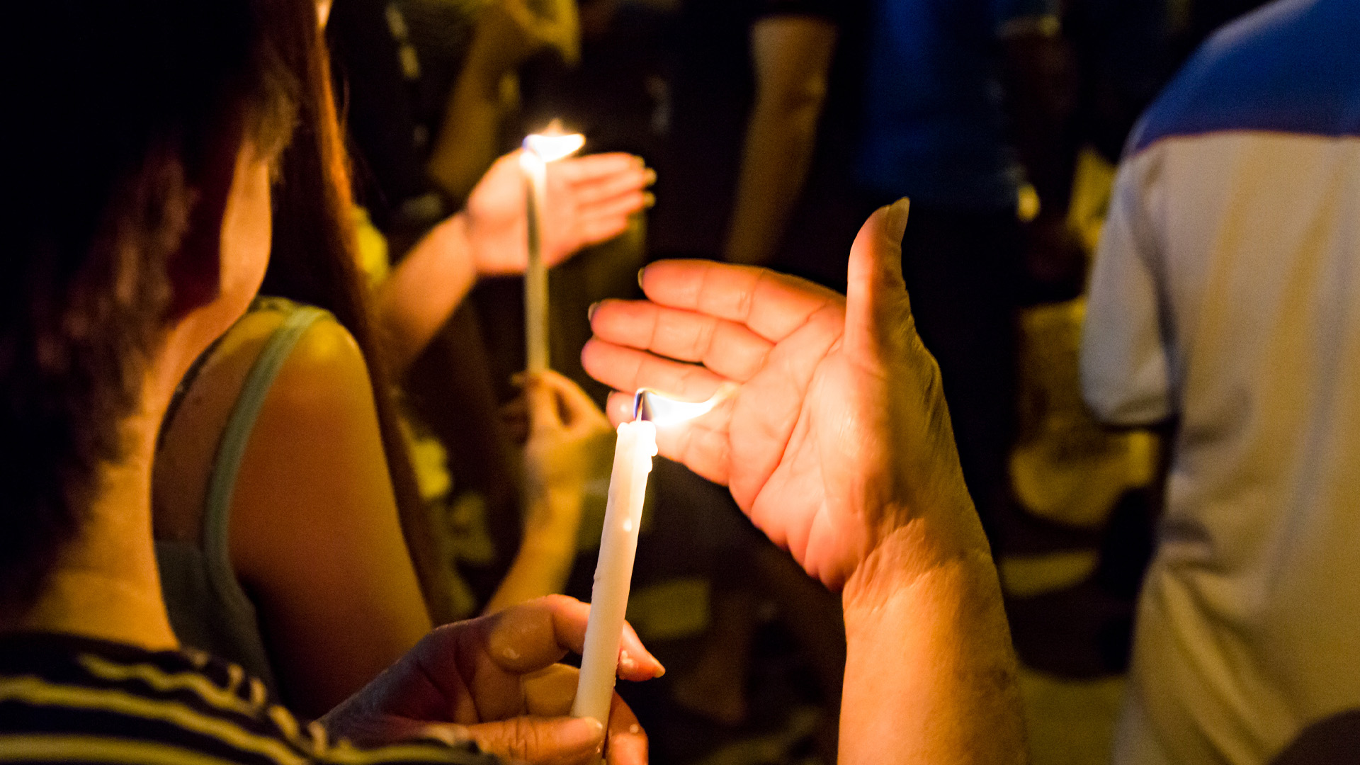 People shelter candle flames with their hands during an evening vigil