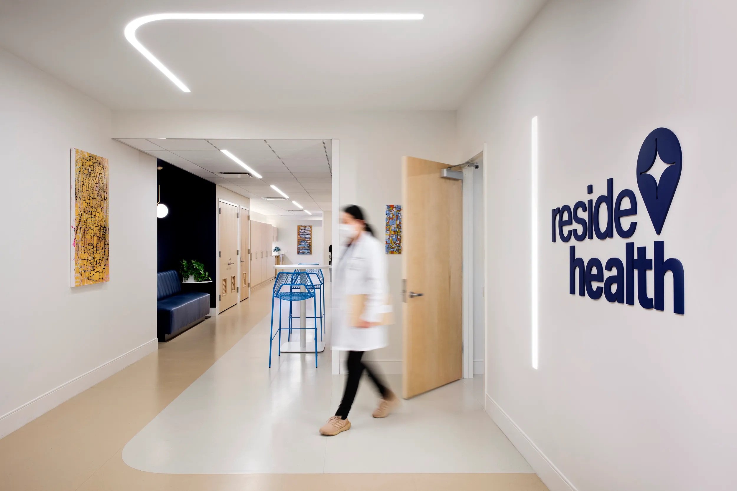 Reside Health clinic interior with curved ceiling lighting, artwork and a clinician walking down the corridor