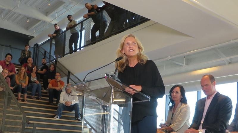 Nancy Kramer speaking at the opening of Resource/Ammirati’s Columbus headquarters, with colleagues gathered on the stairs and balcony
