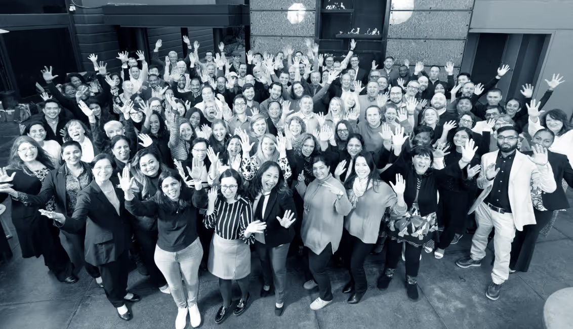 Reveleer employees gathered for a company team photograph, smiling and waving