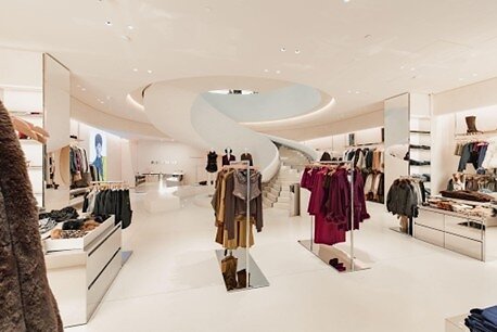 Clothing rails around a sculptural white spiral staircase in REVOLVE’s Grove store