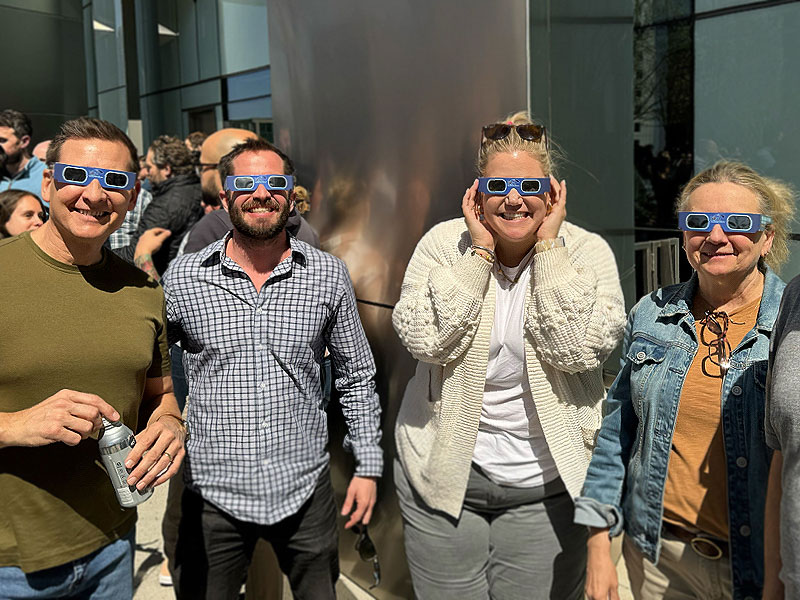 Four Rewards Network team members wearing eclipse-viewing glasses outside