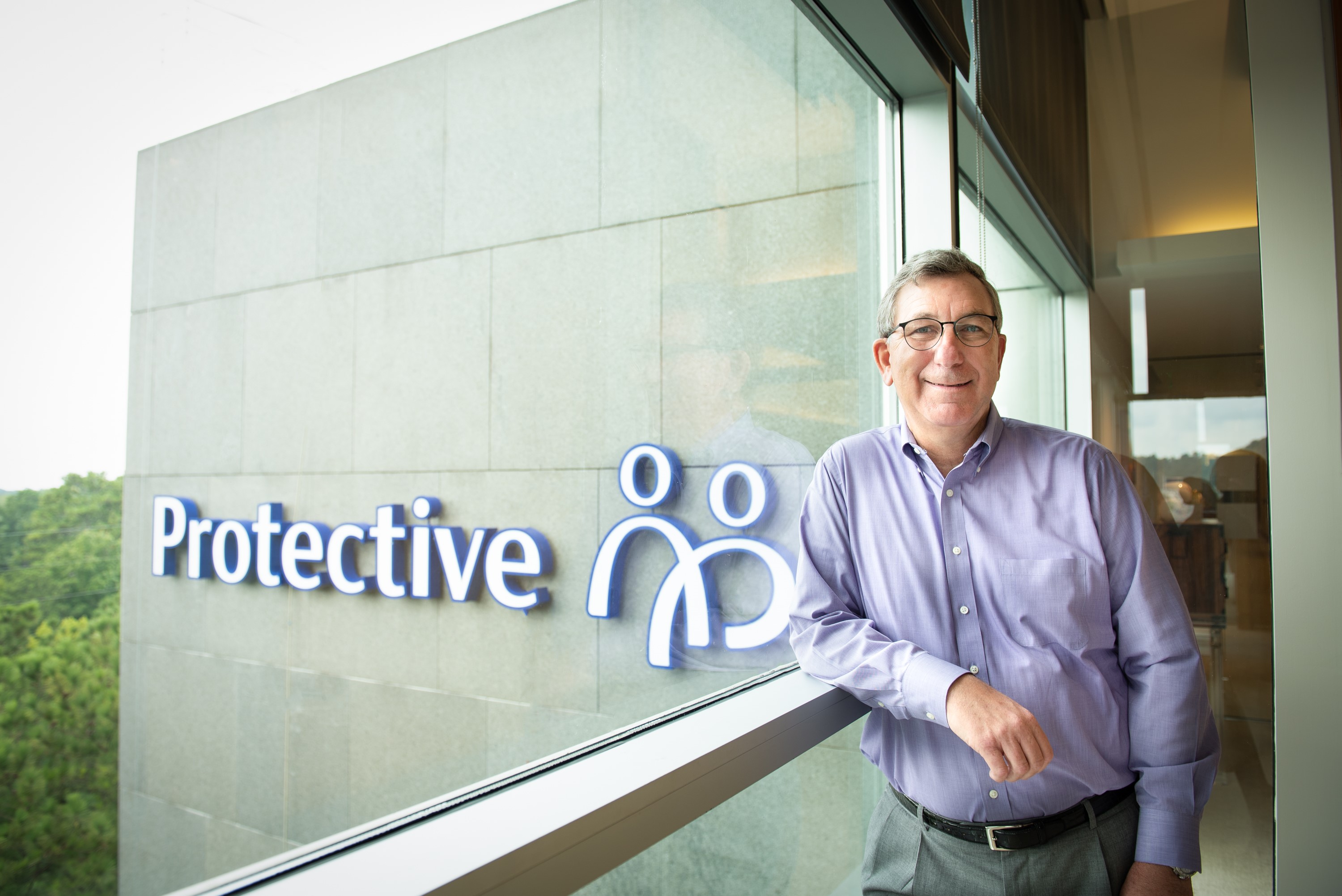 Rich Bielen beside a window at Protective headquarters, with the company’s new logo visible outside