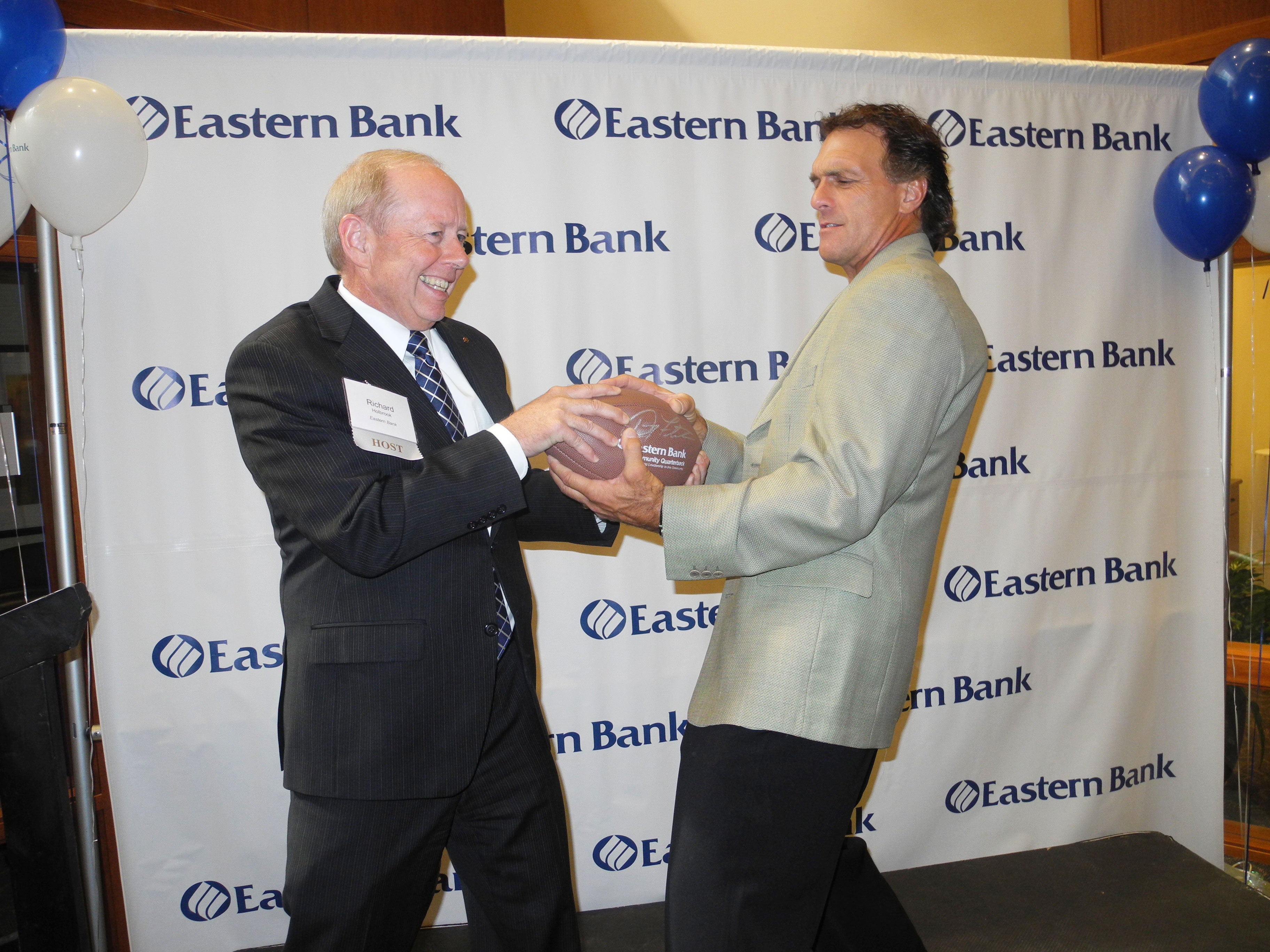 Rich Holbrook, left, smiles while he and Doug Flutie hold a football at Eastern Bank’s 2013 nonprofit celebration.
