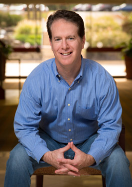 Rich Milgram seated and smiling in a blue shirt