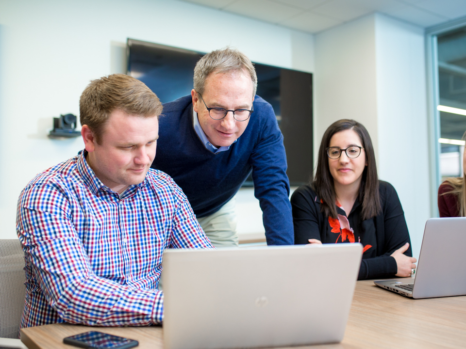 Richard Burke leaning over a laptop while working with colleagues at Envoy Global