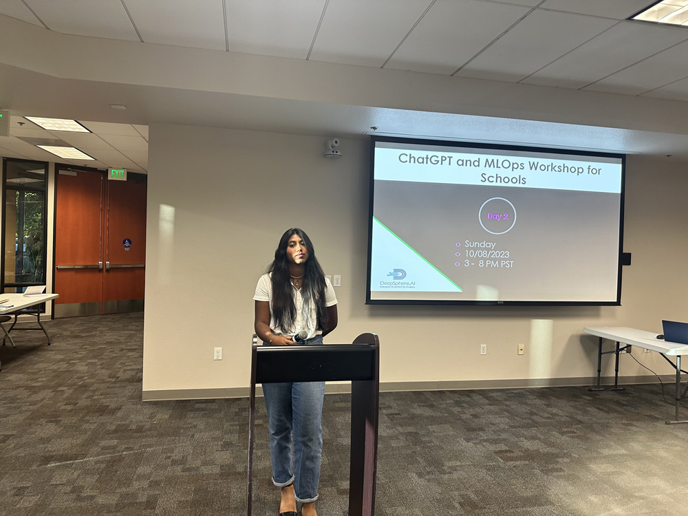 A presenter stands beside a screen for the October 2023 ChatGPT and MLOps Workshop for Schools.