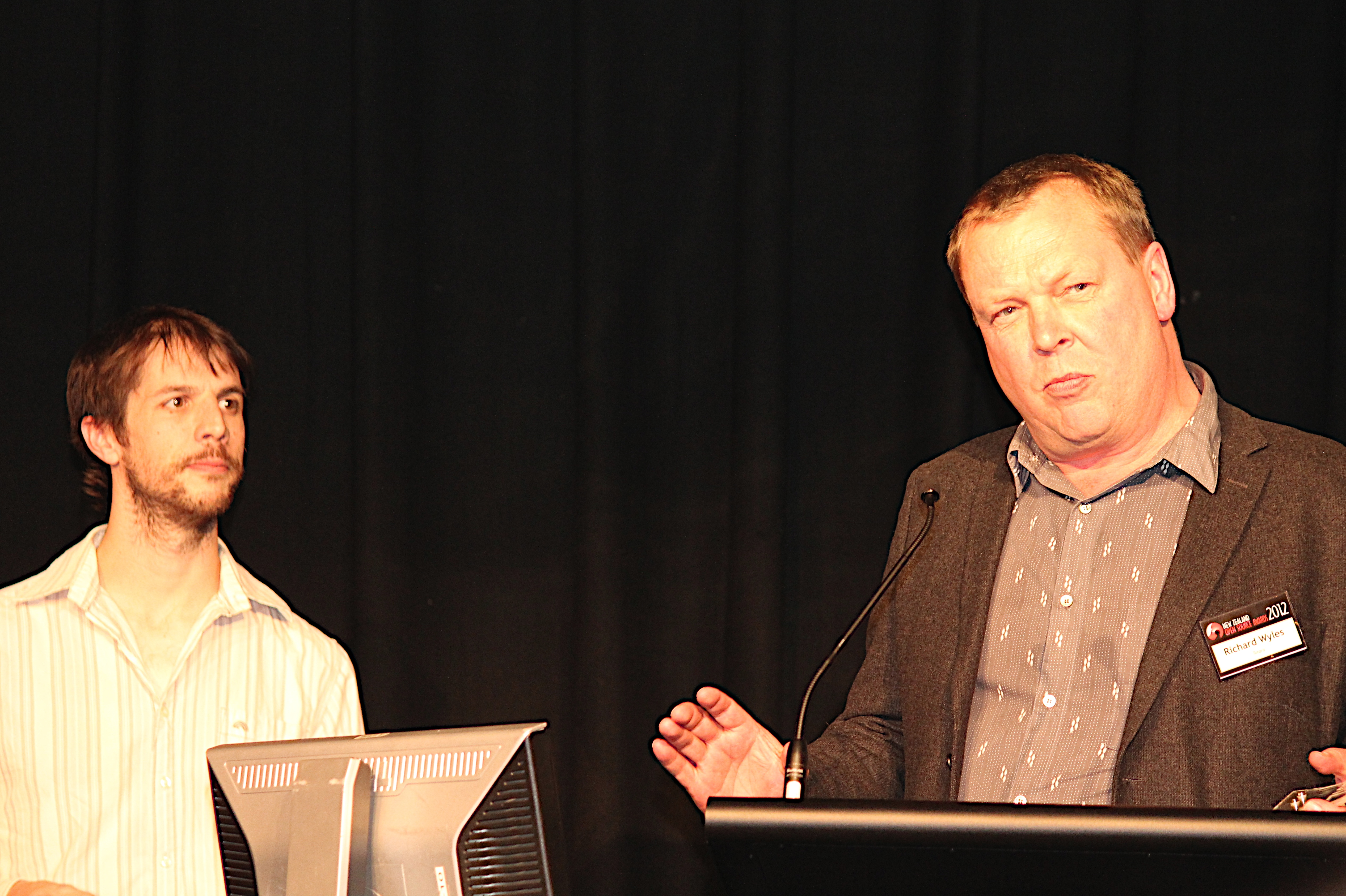 Simon Coggins and Richard Wyles at the 2012 New Zealand Open Source Awards, with Wyles speaking at the lectern.