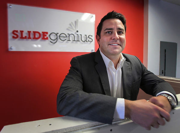 Rick Enrico leaning on an office partition beside a SlideGenius sign