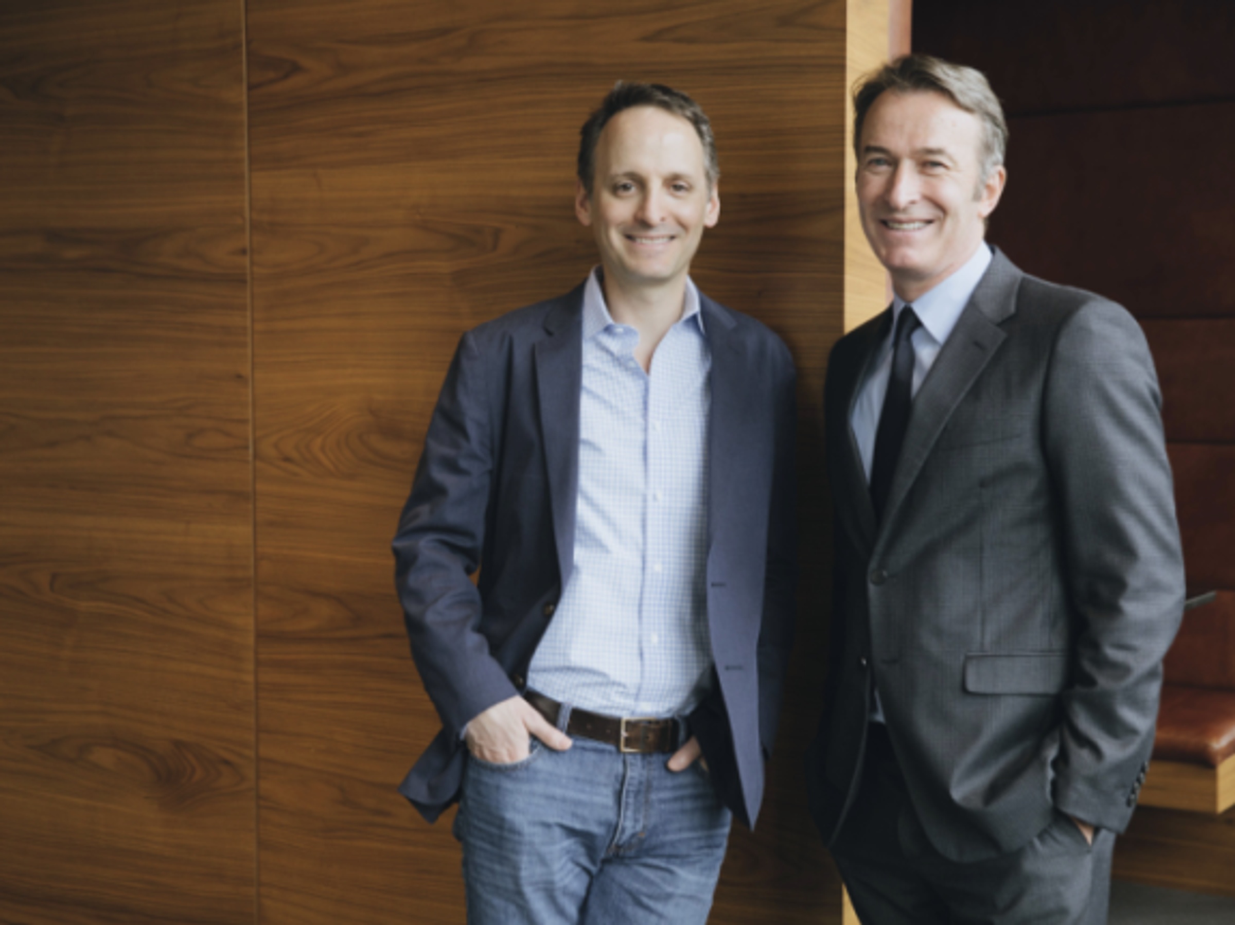 Rick Greenberg, left, and Michael Birkin smiling together against a wood-paneled wall