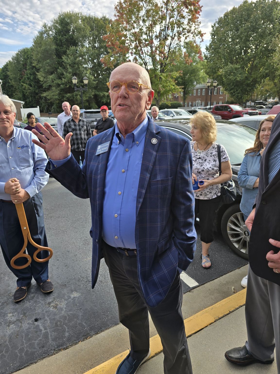 Cornelius Mayor Woody Washam speaking outside the new bank office; ceremonial ribbon-cutting scissors at left