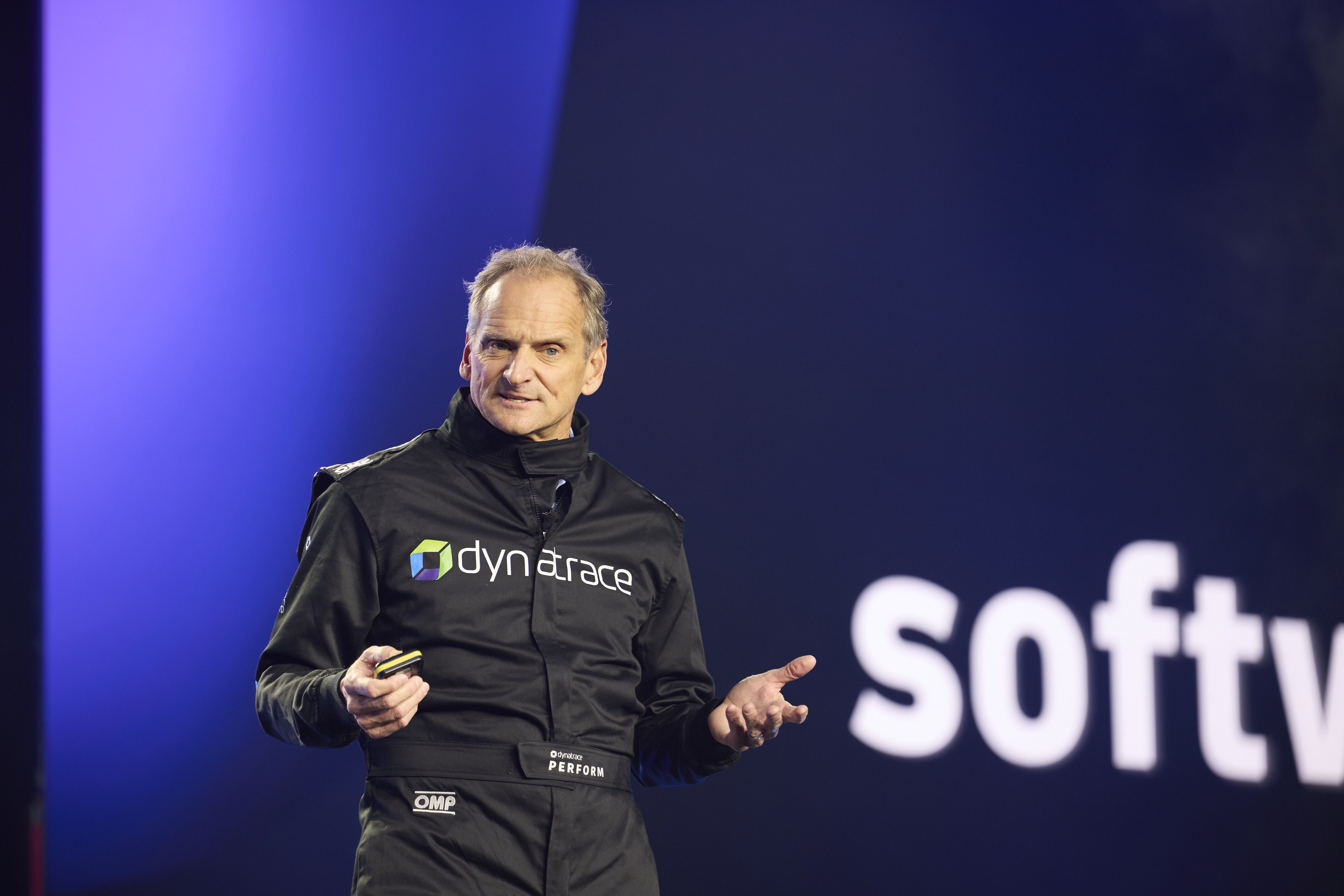Rick McConnell speaking on the Perform 2025 stage in a black Dynatrace racing suit