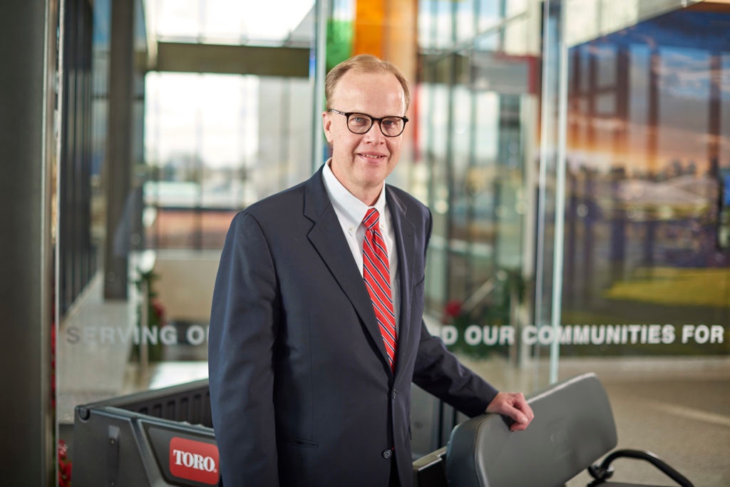 Rick Olson standing beside Toro equipment in a glass-walled corporate lobby