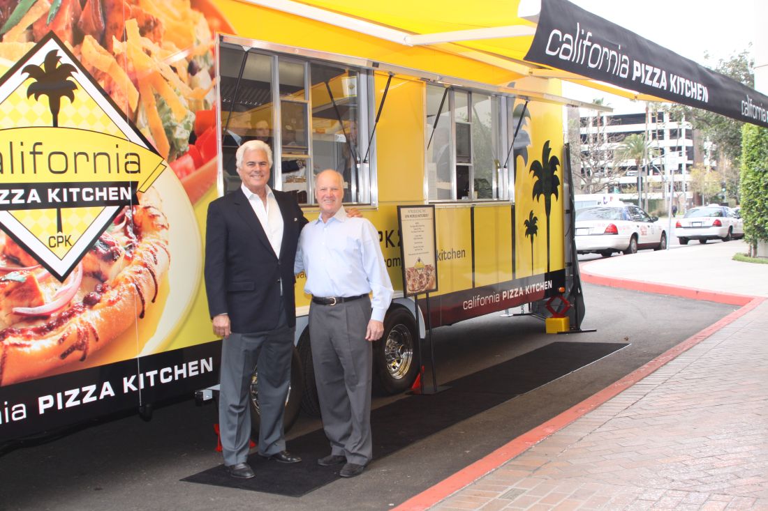 Larry Flax, left, and Rick Rosenfield standing beside a yellow California Pizza Kitchen food truck